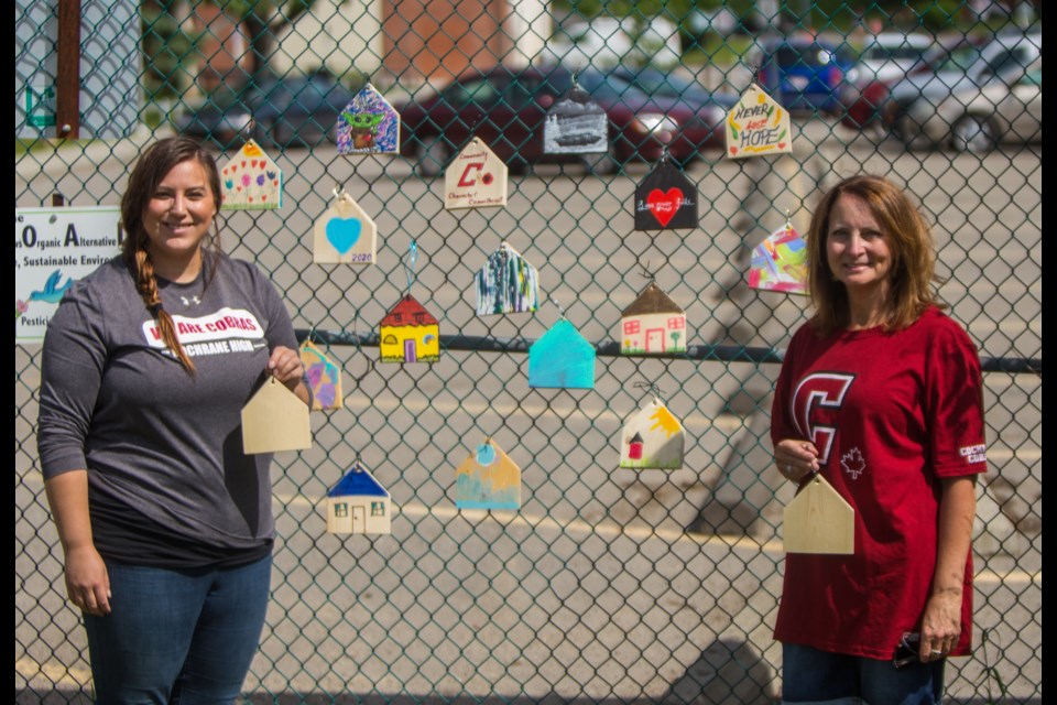 Cochrane High School educators Jasmyne Hazelwanter, left, and Lauraine Laudel show off painted tiny houses that are part of the Hope for Home project Thursday (June 25). (Chelsea Kemp/The Cochrane Eagle)