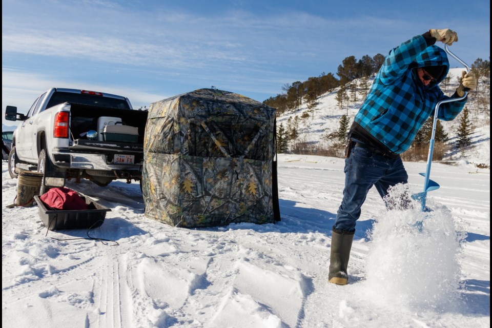 Asa Leslie drills a hole for ice fishing at Ghost Lake on Monday (Feb. 15). (Chelsea Kemp/The Cochrane Eagle)