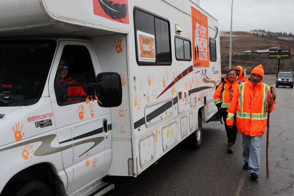 River Steele, left, waits for Virgil Moar, Jazz Lavallee and Vernon Dustyhorn to catch up to their support vehicle in Morley Oct. 29. The vehicle is covered in orange handprints of children they have met along their walk from Winnipeg to Kamloops raising awareness for residential schools. (Jessica Lee/The Cochrane Eagle)