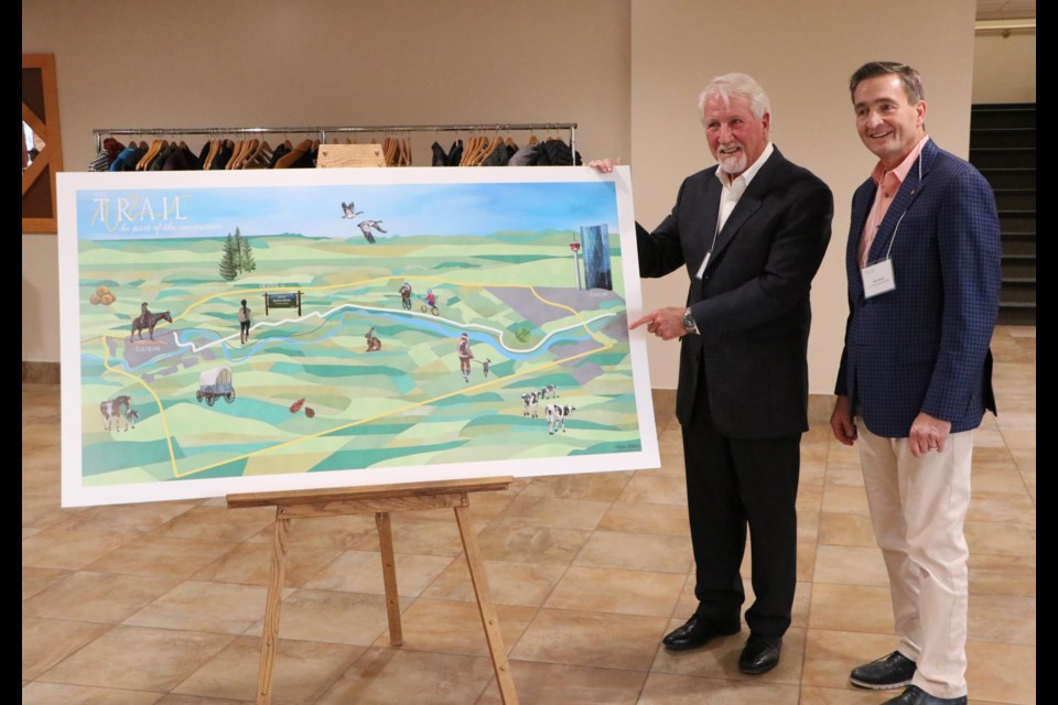 Trail Steering Committee member Daniel Kroffat, left, and commitee chair Alex Baum unveil the artist's rendering of what the trail from Cochrane to Calgary could look like at the RancheHouse Nov. 30. (Jessica Lee/The Cochrane Eagle)