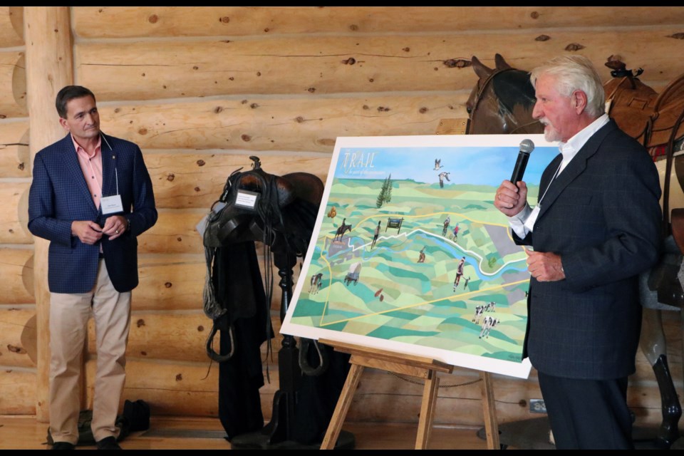 Trail Steering Committee chair Alex Baum, left, and committee member and capital fundraiser Daniel Kroffat unveil the artist's rendering of what the trail from Cochrane to Calgary could look like at the RancheHouse Nov. 30. (Jessica Lee/The Cochrane Eagle)