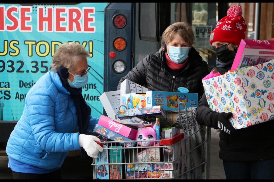 Activettes members push a cart chock-full of donations toward the toy bus set up for transport to their Share Your Christmas Hamper workshop Dec. 11. (Jessica Lee/The Cochrane Eagle)