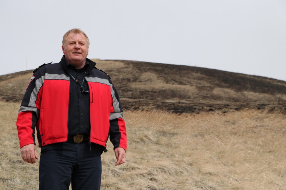 Cochrane Fire Services inspector Jeff Avery stands in front of a hill at Dewey Blaney Park April 13, where a grass fire burned through the area last week. (Jessica Lee/The Cochrane Eagle)