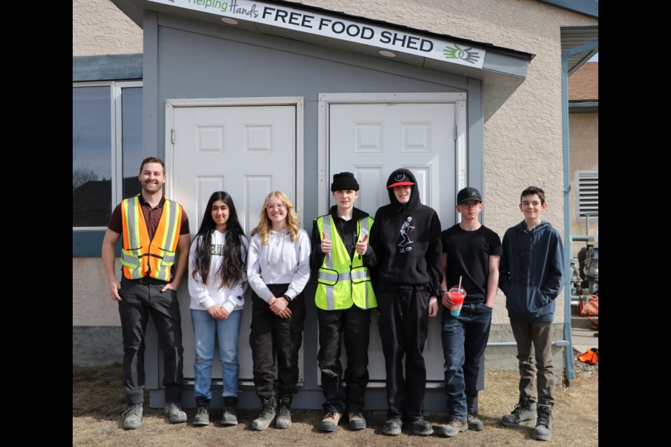 Dave Pedersen, a teacher with Rocky View Schools' Cochrane Learning Centre Building Futures program and students with the program pose for a photo in front of the second Helping Hands Free Food Shed at Bow Valley Baptist Church March 22. (Jessica Lee/The Cochrane Eagle)