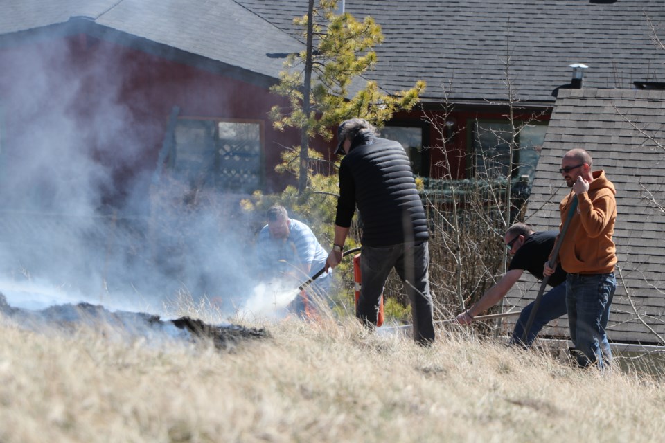 Resident in the area used fire extinguishers, buckets of water, garden hoses, rakes and brooms to put out a grass fire on the hill by homes near Dewey Blaney Park April 8. (Jessica Lee/The Cochrane Eagle)