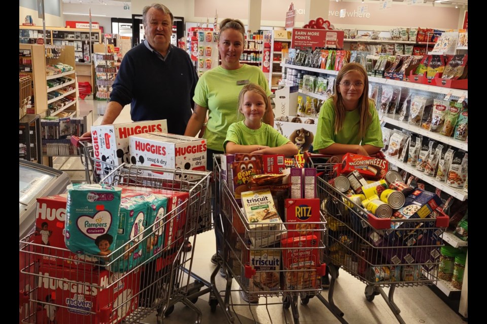 Keith Johnson, left, redeemed 670,000 PC Optimum points in purchases at Shoppers Drug Mart Aug. 24 in support of the Helping Hands Society of Cochrane and Area. Food security programs manager with the non-profit, April Baird, right, and her daughters Ashtyn and Addison, were on hand to help shop the items to be used for stocking the free food sheds, for their Meal Teams program and for contributing to the Cochrane Activettes food bank.