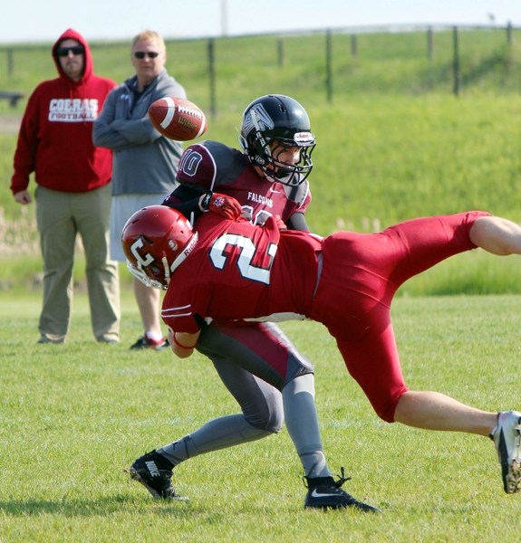 Cochrane High School Cobras linebacker Ethan Forrest delivers a ball-jarring tackle as coaches (back, from left) Seth Henderson and Jeff Avery observe approvingly at Holy