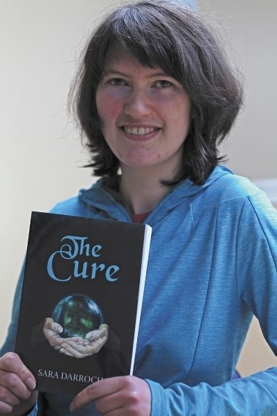 Sara Darroch, a local author, poses with her first book, The Cure. Darroch began writing The Cure in 2009 and put the final touches on it in 2014.