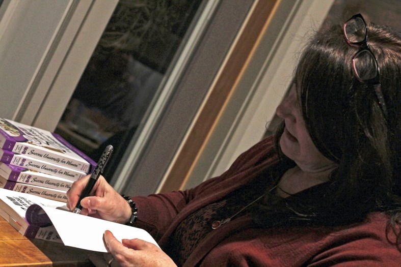 Catherine Scheers, co-author of Success University for Women, signs a copy of the book during an event at The Cave, Sauna Day Spa &#038; Bistro on March 1.