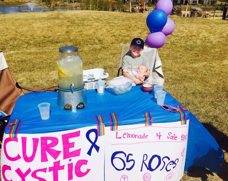 Seamus Dillon holds his baby sister, Georgia, at one of his weekly lemonade stands in Cochrane.