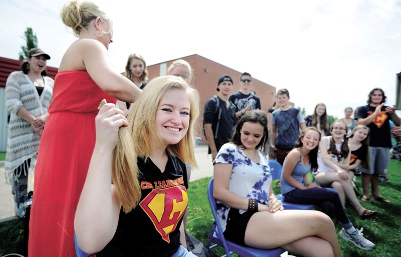 Cochrane High School student Sophie Nicholson holds some locks of her hair taken off by Alicia Morgan of Sublime Styles Hair and Esthetics while her schoolmates watch and