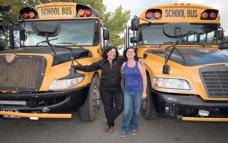 Bus driver Tanya McNeill, right, and her boss Kathy Fenton pose for a portrait with Fenton&#8217;s buses at Cochrane High School.