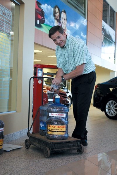 Alex Baum of Cochrane Toyota dumps pennies into jugs at the dealership on the old-fashioned weigh scale that will be used to weigh pennies by the pound at ATB Financial Sept. 