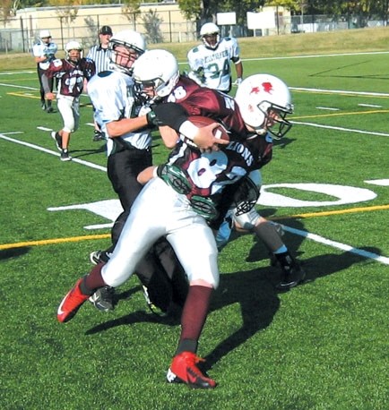 Cochrane Lions receiver Cole Avery fights for yards against Calgary Hilltoppers defenders as teammate Michael Scott lays a crushing block in Calgary Bantam Football