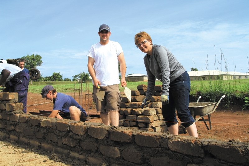 From left; Kerri Friesen, Cochrane firefighter Josh Tait and Lorie Gordon lay bricks for the nursery.