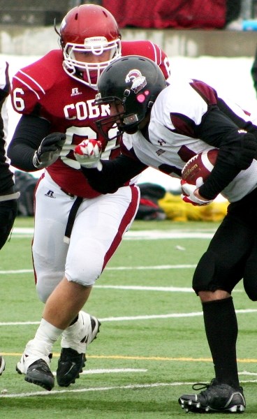 Cochrane High School Cobras defensive lineman Bryce McKinnon (left, about to introduce himself to the earhole of Rundle College Cobras running back Noah Muruve during 2012