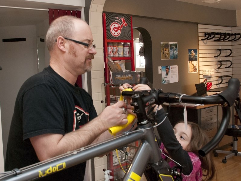 Dan Richter tapes up the handle bars of road bike with the help of his six-year-old daughter, Danica. Richter and his family own and operate the newly opened Cafe Roubaix