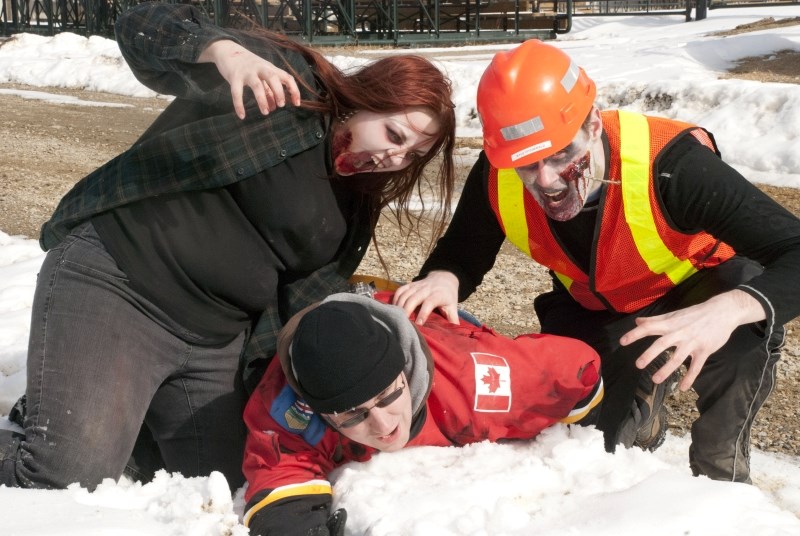 Zombies Lindsay Moreland and Kyle Fitzgerald prepare to attack fallen Flames fan James Rooke during filming for Zombie Survivor at the Cochrane Ag Society March 10. Zombie