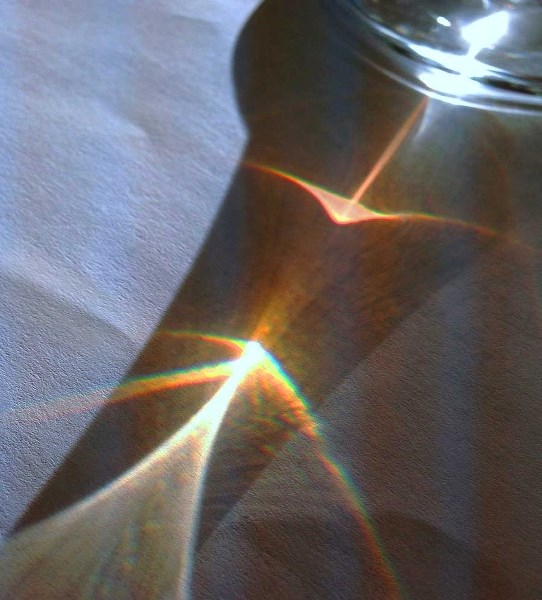 Glass of water refracting sunlight onto paper is like us as agents of Beauty in the world.