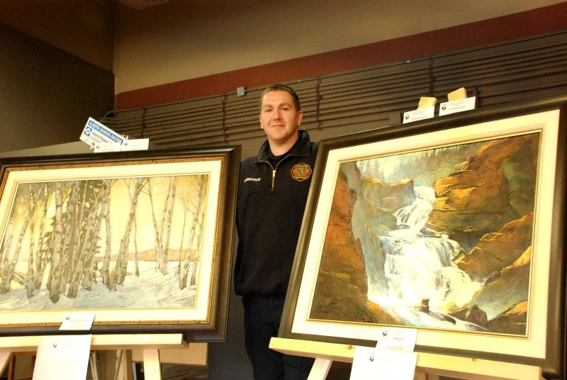 Gary Robertson, of the Redwood Meadows Firefighters&#8217; Association, shows off two David Langevin paintings that are being offered up as part of the charity&#8217;s art