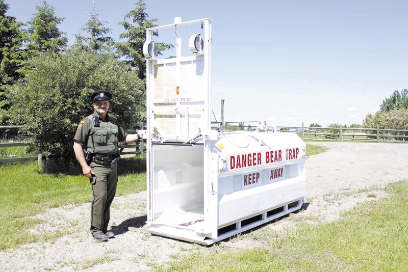 Fish and Wildlife officer David Dickson stands next to a bear trap set in Rolling Range resident, Elaine Wood&#8217;s yard. Wood spotted a grizzly bear trying to get into her 