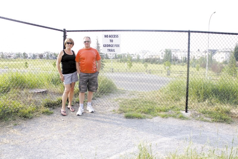 Jumping Pound residents, Mary and David Tomlinson, stand by the six-foot fence the town recently put up to prevent area residents from using the popular path to cross George