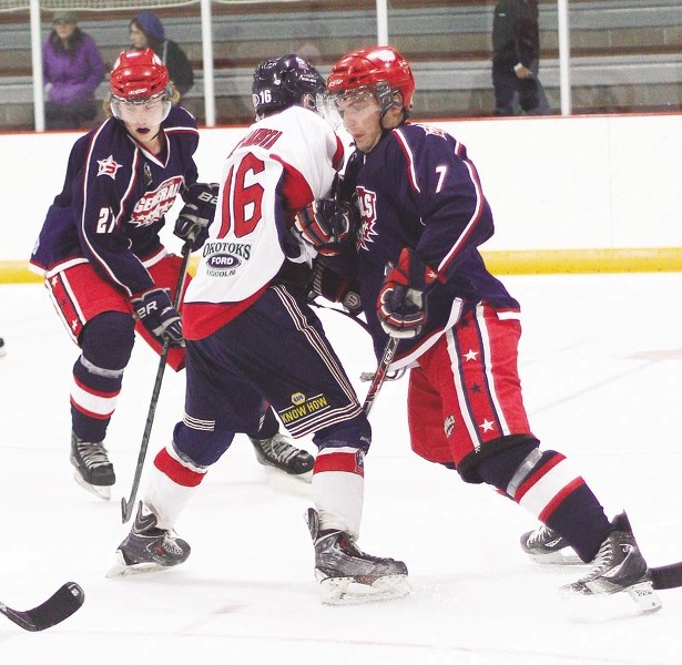 Cochrane Generals veteran defenceman Craig Packard leans into Okotoks Bisons forward Spencer Barlow-Lakusta as Gens defenceman Matt Dunne supports the play at Spray Lake