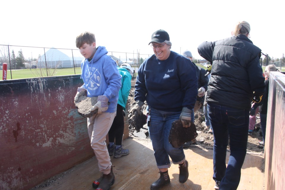 Volunteers helped by hand-bombing chunks of broken-up asphalt from a pile on the ground into a dumpster for recycling.