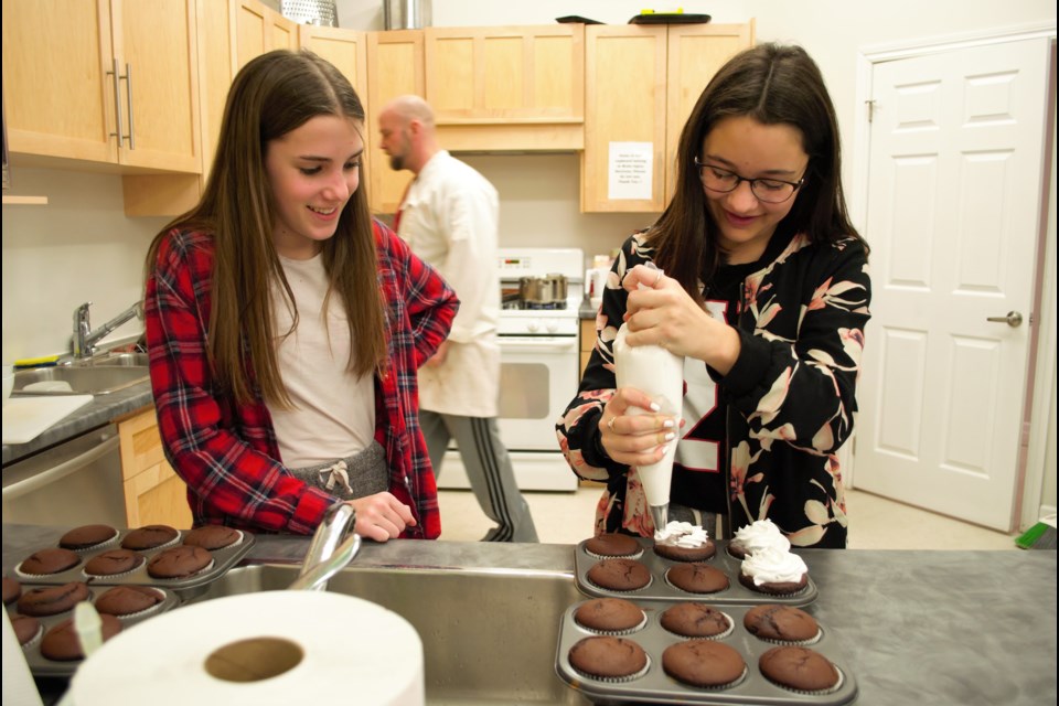 Tegan Menard, 13, watches while Lauren Sholtz, 13, pipes vanilla buttercream icing onto chocolate cupcakes. Jessica Owen/CollingwoodToday