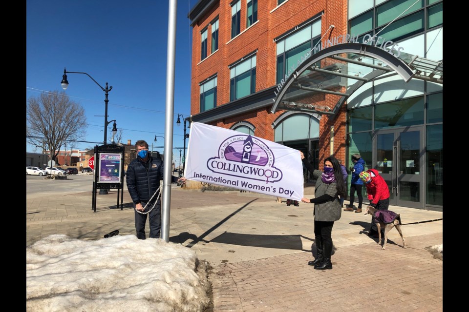 Collingwood mayor, Brian Saunderson, with My Friend's House board chair, Zahra Saigar in front of Collingwood Public Lirbary raising the flag for International Women's Day. 