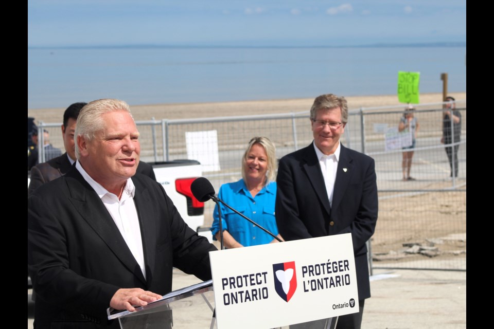 Premier Doug Ford made a $38-million announcement for Wasaga Beach tourism on Friday, while a Bill 5 protester held up protest signs behind him.