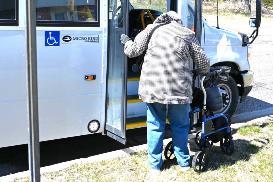 Resident prepares to ascend city bus steps with walker. Apr. 20, 2024