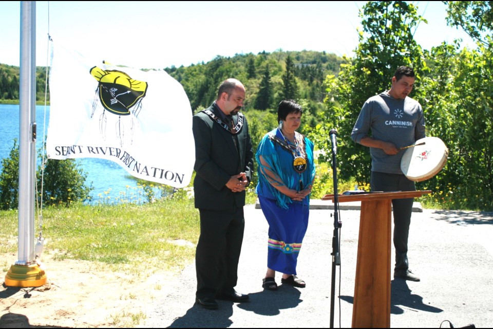 Serpent River First Nation (SRFN) resident Bud Jacobs playing a drum song prior to raising the SRFN flag at its permanent location at Elliot Lake’s Miners’ Memorial. He is joined by Chief Elaine Johnston and Mayor Dan Marchisella. Kris Svela for ElliotLakeToday