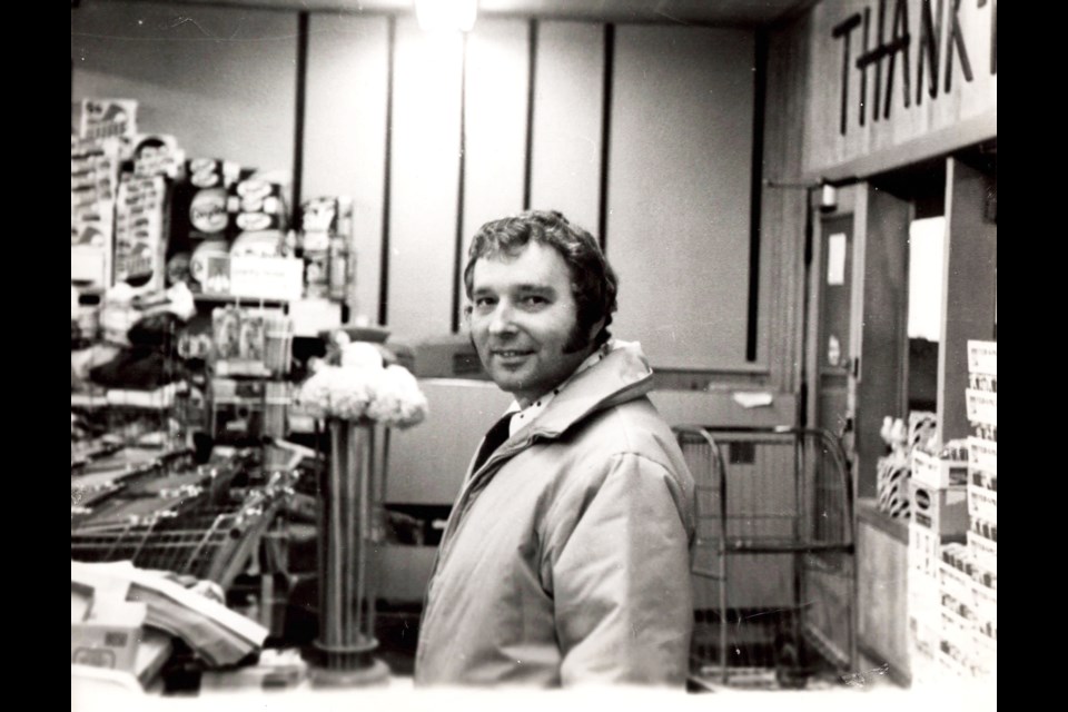 A black and white photo of Merlen Kropf standing in one of the grocery stores he owned.