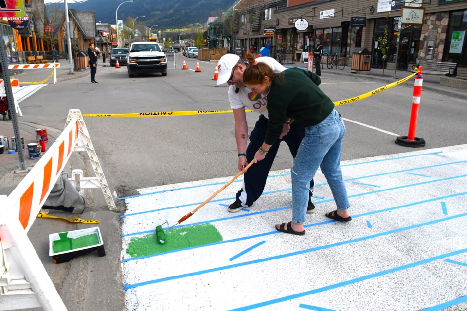 Mychol Ormandy, executive director of OUT Jasper, and volunteer Krista Gillese begin painting the rainbow crosswalk outside of TD Bank in Jasper on Thursday, May 30, 2024. | Peter Shokeir / 51