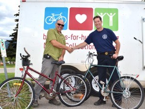 Paul Paridaen and Greg Van Tighem shake hands shortly before tossing the first donated bikes into the Bicycles for Humanity Trailer. Trevor Nichols photo