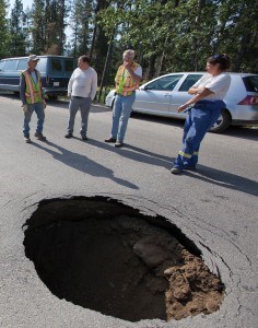 A Sinking Feeling: Members of a municipal utilities crew keep an eye on a sink hole that opened up in the road outside the Bottle Depot in Jasper's industrial park on Wednesday morning, July 11. After waiting for below-ground gas and communications lines to be located, workers began to dig in the loose earth and discovered a surprising cause of the problem. For the story and more photos, please see page 2.