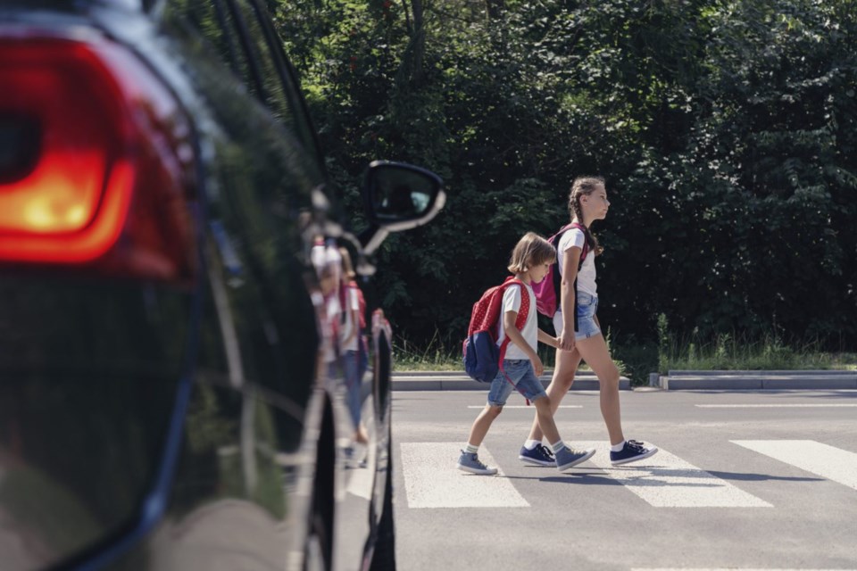 Children next to a car walking through pedestrian crossing to the school