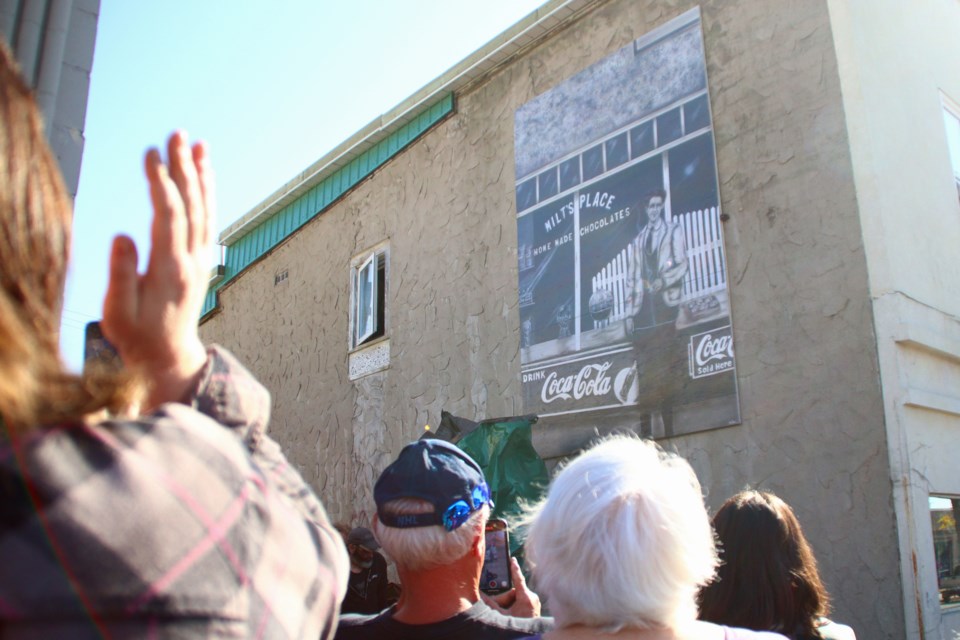 Passersby applaud a new mural on the side of the Uptown Emporium building on Main Street Sept. 22. The mural
shows businessman David “Milt” Young in front of Milt’s Sweet Shop, the confectionery store he used to own at the same site.