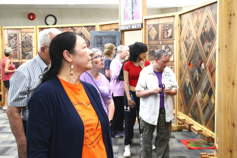 Attendees, including lead organizer Theresa Wride, look over the Witness Blanket exhibit, which features hundreds of photographs and artifacts detailing the history and the damage inflicted by Canada's residential school system.