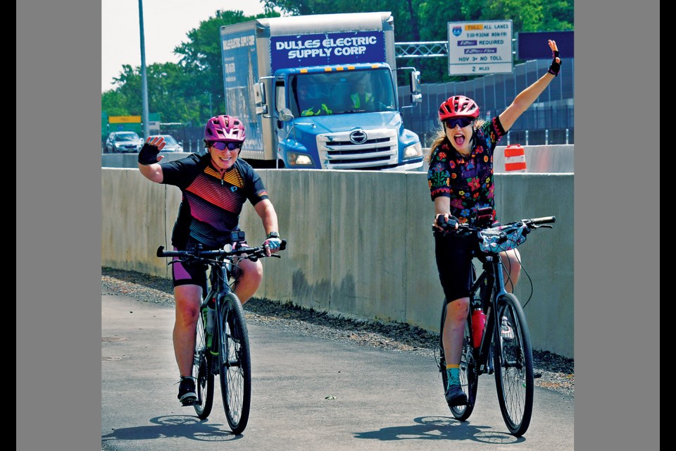 Cheryl Anders and Kari Cannistraro wave while riding bicycles along the newly opened initial sections of the I-66 Parallel Trail in Vienna on May 17, 2023.