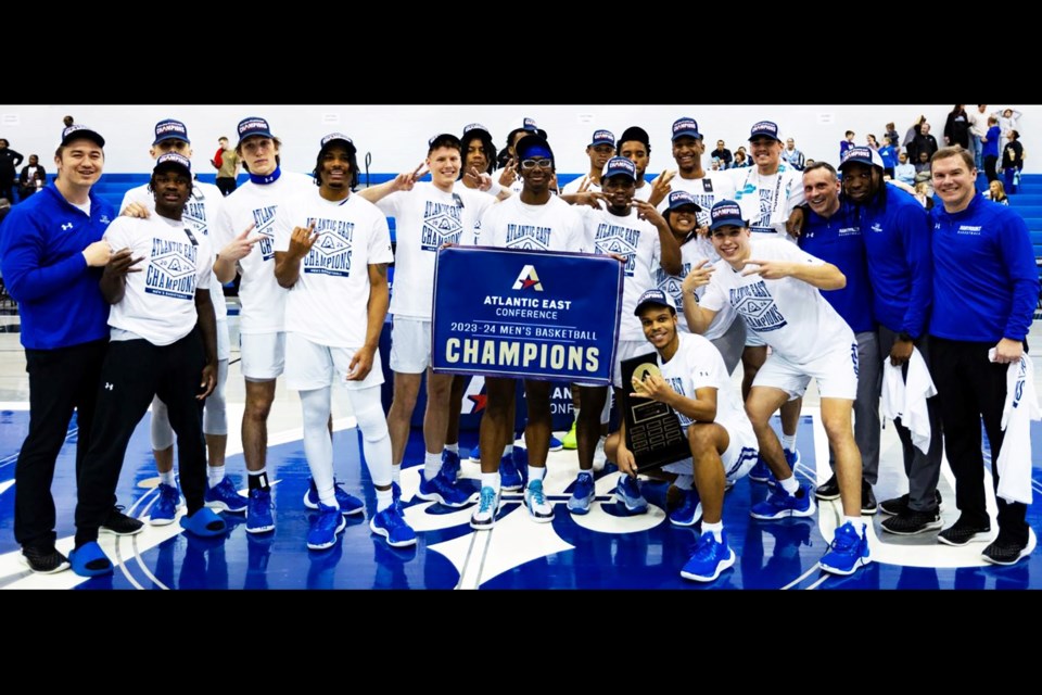 The Marymount University men's basketball team gathers with the conference-tournament championship banner and trophy.