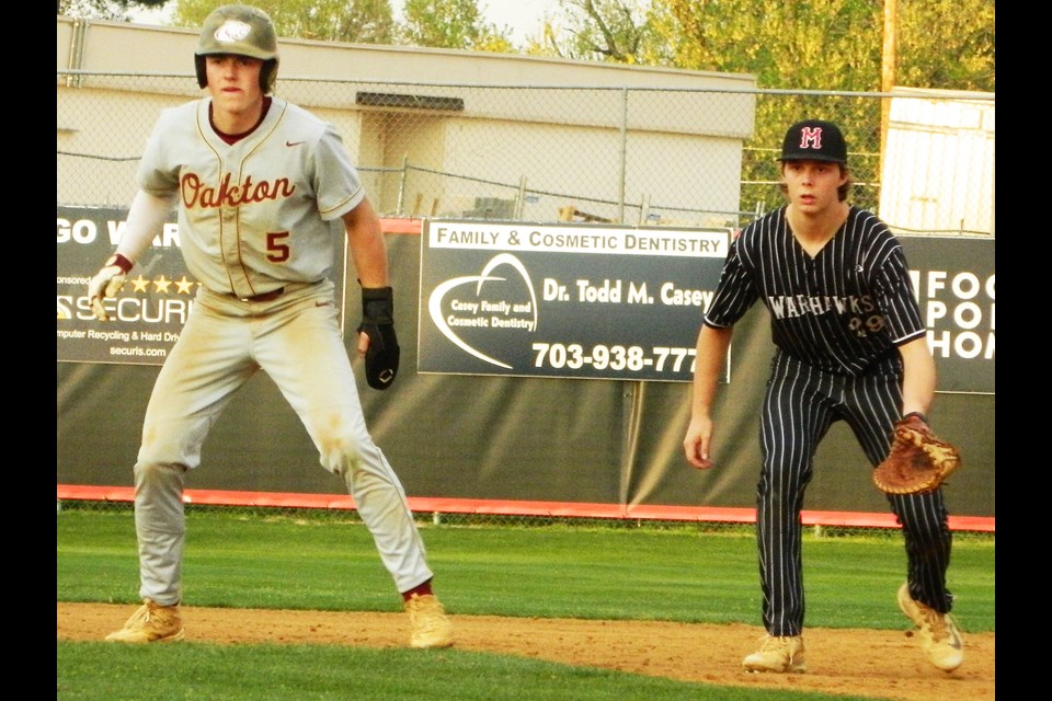 Oakton's Noah Toole takes a lead off first base as Madison's Nathan Tondreault eyes the runner.