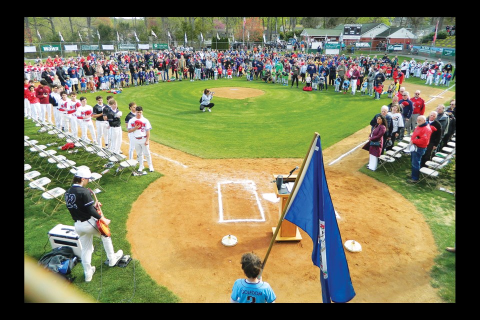 Madison High School baseball player’s Jackson Bourdeau, bottom left, plays the national anthem at Vienna Little League’s opening day as many watch.