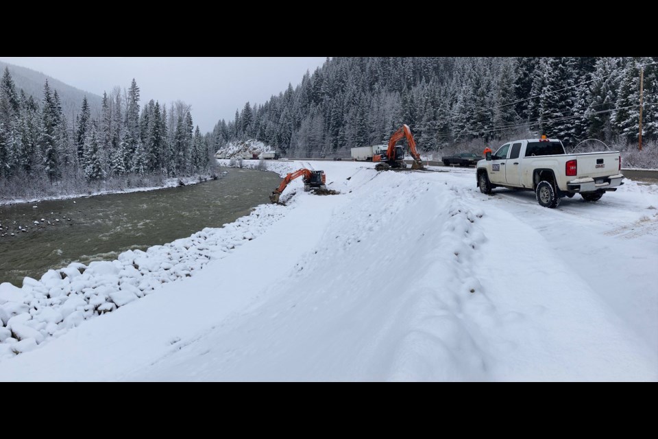 An excavator passes riprap down to the other on a lower bench, building an erosion control embankment, along Highway 3.