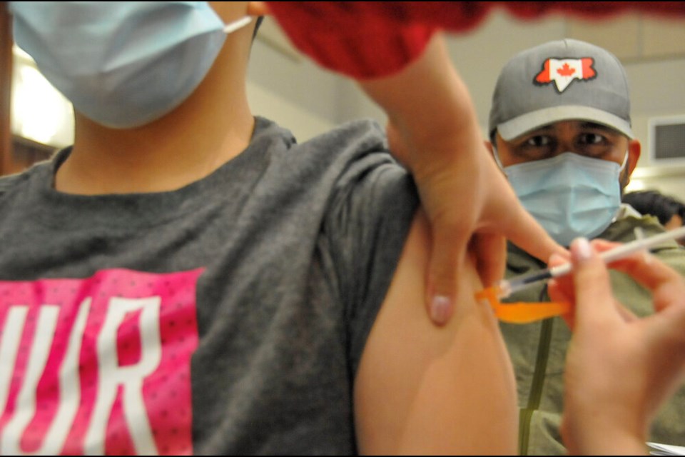 Nahun Navarro watches his son, 12-year-old Romeo, get his first dose of the COVID-19 vaccine.