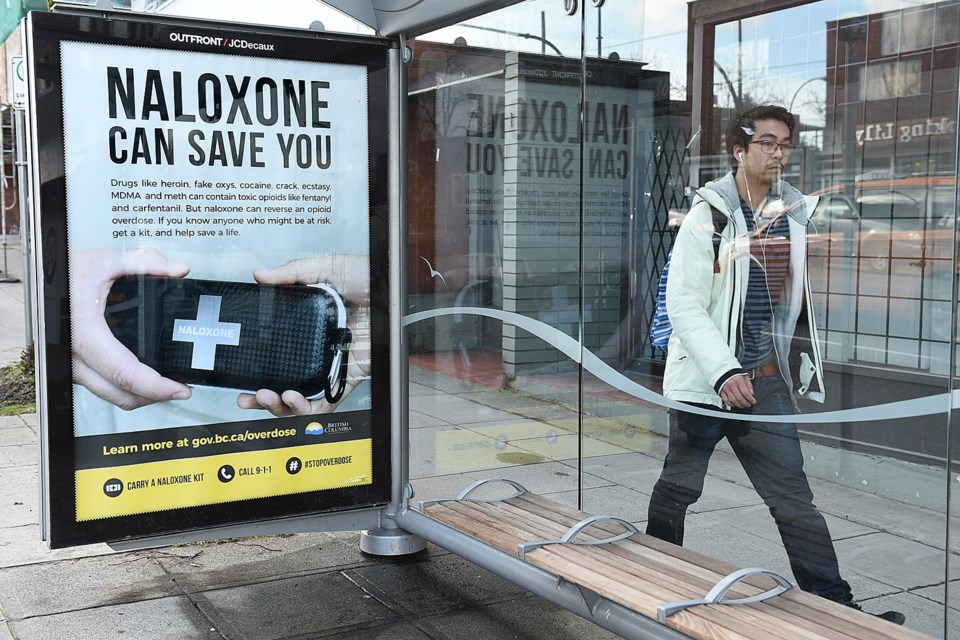 A man walks past a Vancouver bus shelter with a poster promoting naloxone kits. Photo Dan Toulgoet