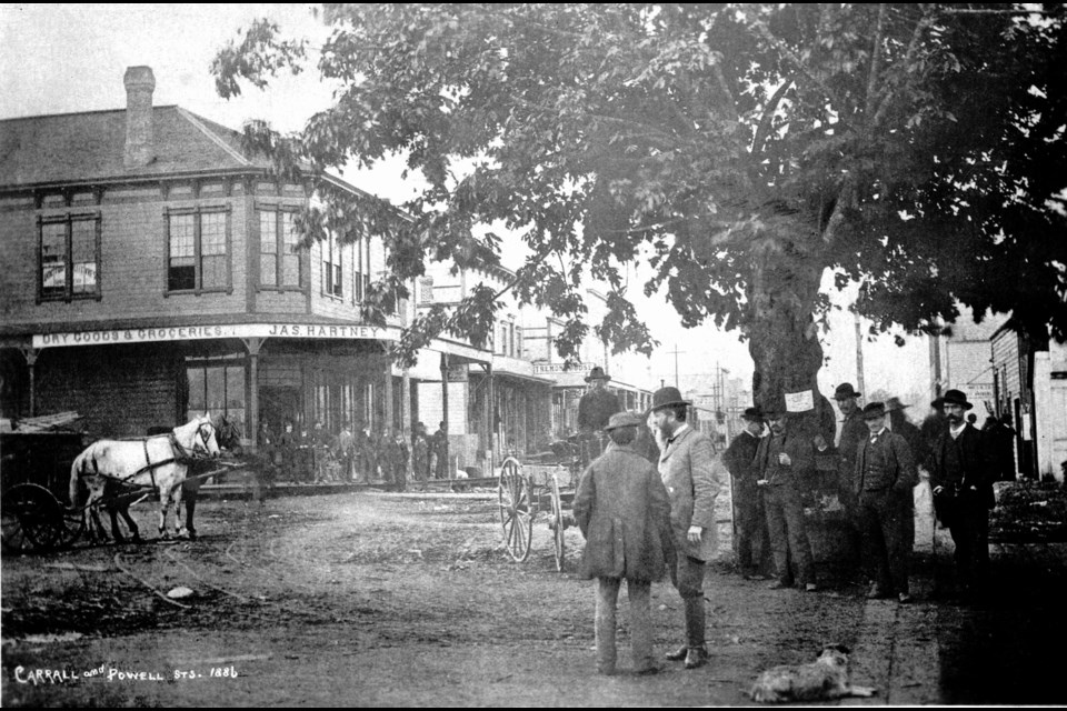 A group of men stand around the old maple tree in Gastown in 1886. The photo was taken at Water and Carrall Street, with the steps of the old Deighton House Hotel at the far right. PHOTO City of Vancouver archives