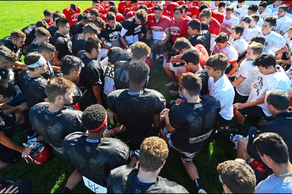 Members of the St. Thomas More Knights varsity, junior varsity and Grade 8 football teams gather on the field prior to practice Monday in a prayer for head coach Bernie Kully who died Saturday.