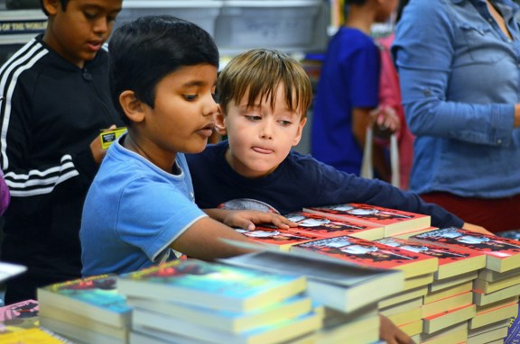 Maywood Community School Grade 2 students Saketh and Novak peruse stacks of books at their school library Tuesday. Thanks to a donation of 4,000 new books, each student at the school was allowed to pick five books to take home and keep.